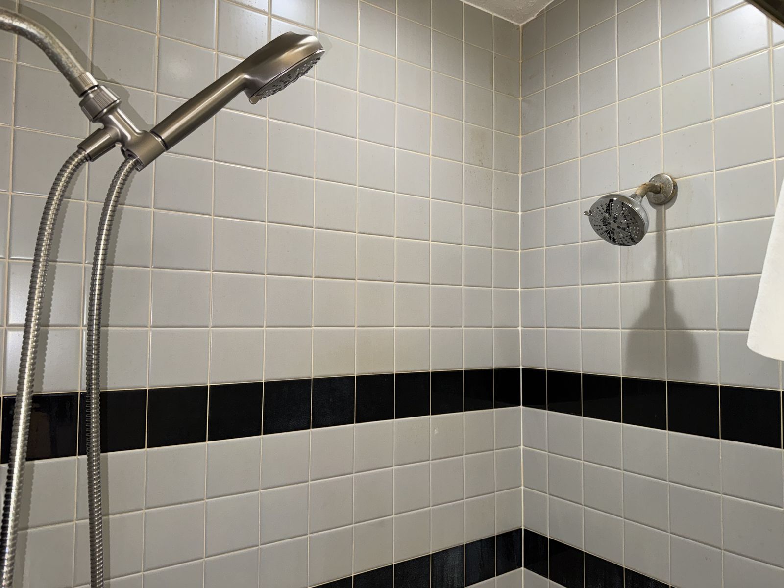 New shower head and handheld sprayer installed on tiled shower wall